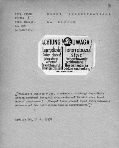 Tablica z napisem w języku niemieckimi i polskim informującym o zakazie fotografowania pod groźbą zastrzelenia. Tablice o takiej treści były umieszczane na ogrodzeniach obozów koncentracyjnych.